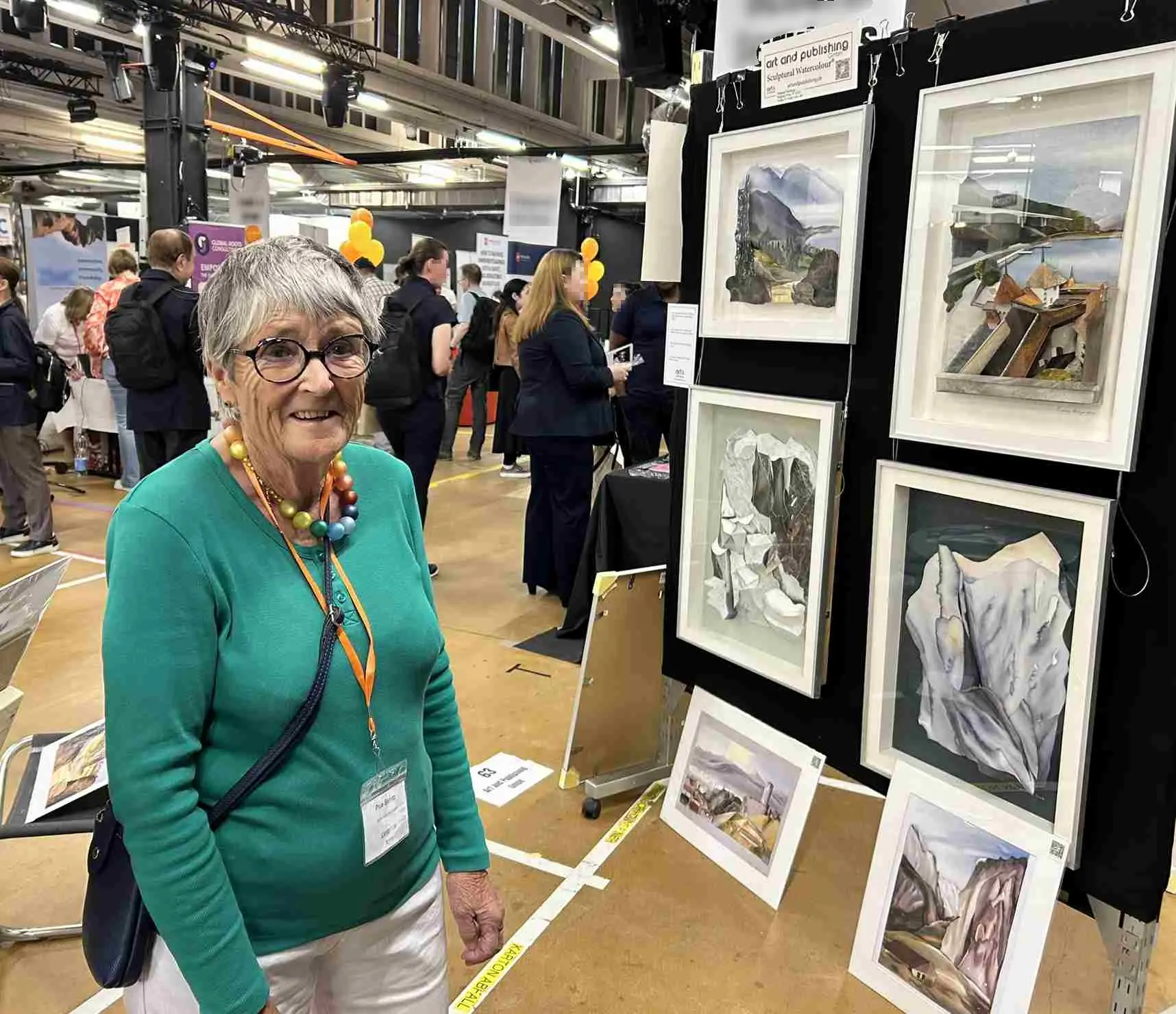 Artist Prue Bishop at her stand at Expat Expo Zug 2025, with original Sculptural Watercolour® paintings on display